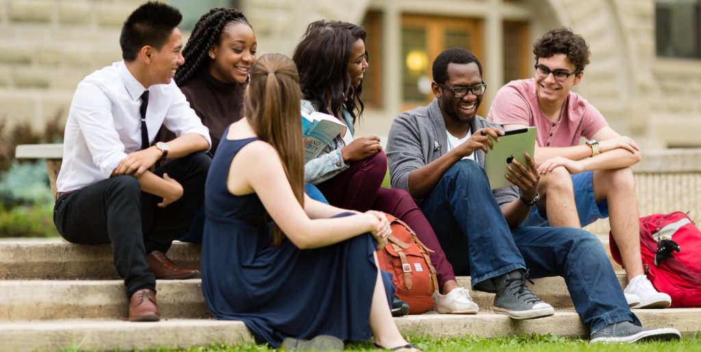 international students sitting on a lawn looking atheir books and tablets discussing their curriculm and exams